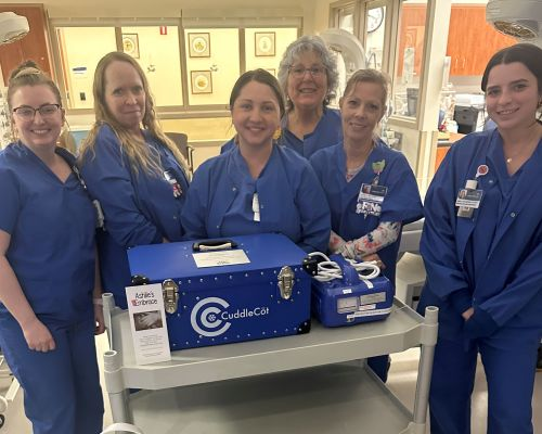 Hospital nurses gather around a CuddleCot provided through Ashlie’s Embrace to support families experiencing stillbirth and infant loss.